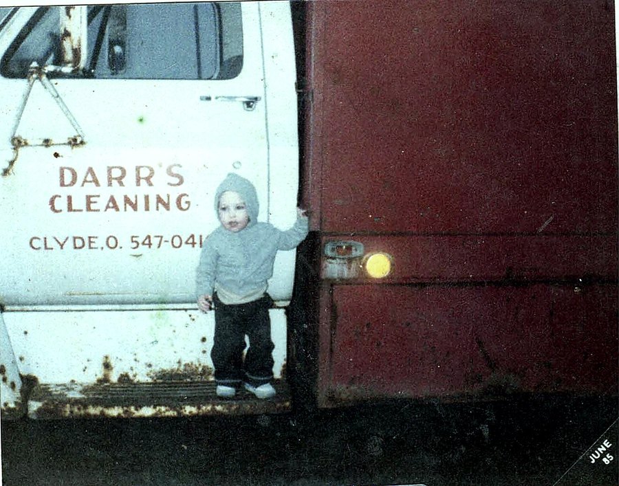 A small child standing on the step of a Darr’s Cleaning truck, dated June 1985