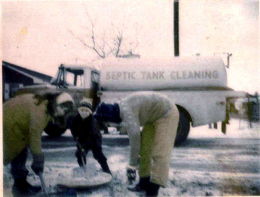 Crew digging around a septic lid in the snow with a Septic Tank Cleaning tanker behind