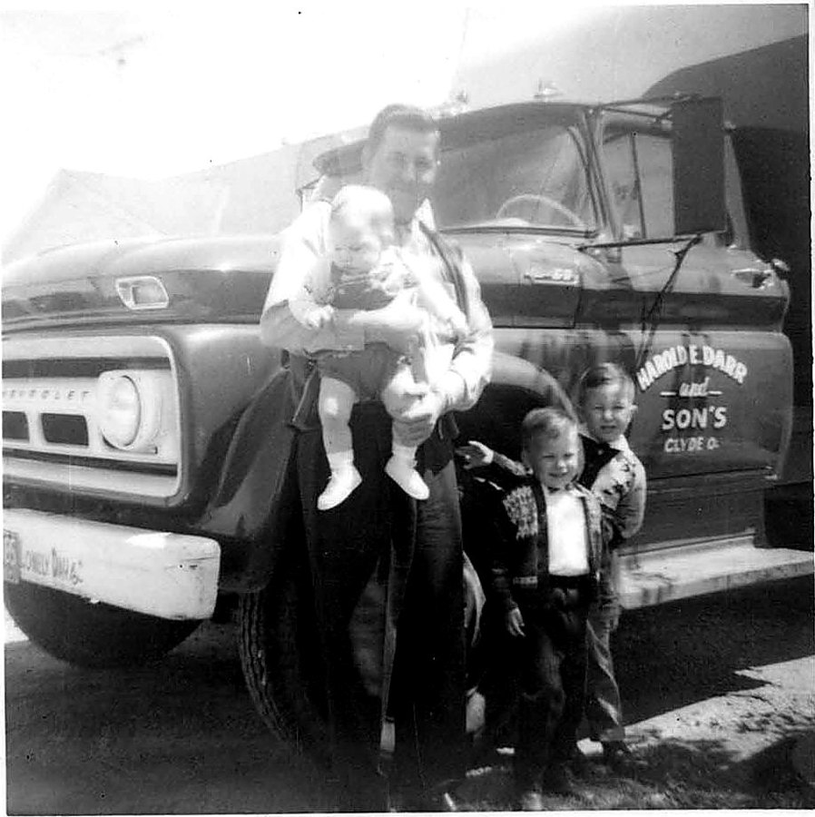 Harold Darr holding one of his sons beside a truck lettered Harold E. Darr and Sons, Clyde O.