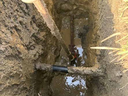 A narrow hydrovac excavation with a buried service uncovered intact at the bottom, the sides of the hole cut clean