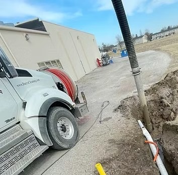 A Darr's vacuum truck with its suction hose running down into an open excavation beside a building