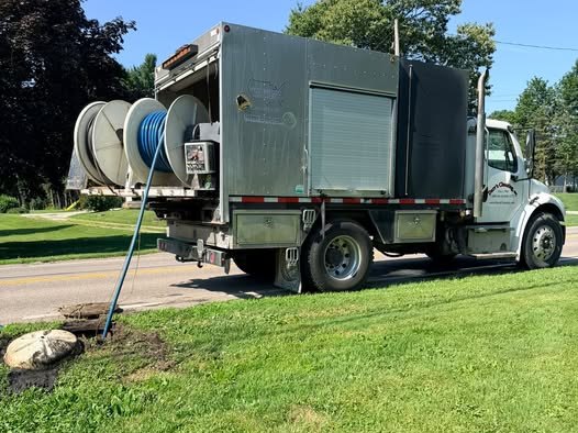A Darr's jetting truck at the roadside with its hose reels, working a line through a structure beside the road