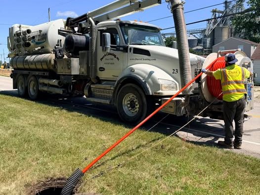 A Darr's Jet-Vac combination unit parked at an open manhole with a crew member in high-visibility clothing feeding the hose in