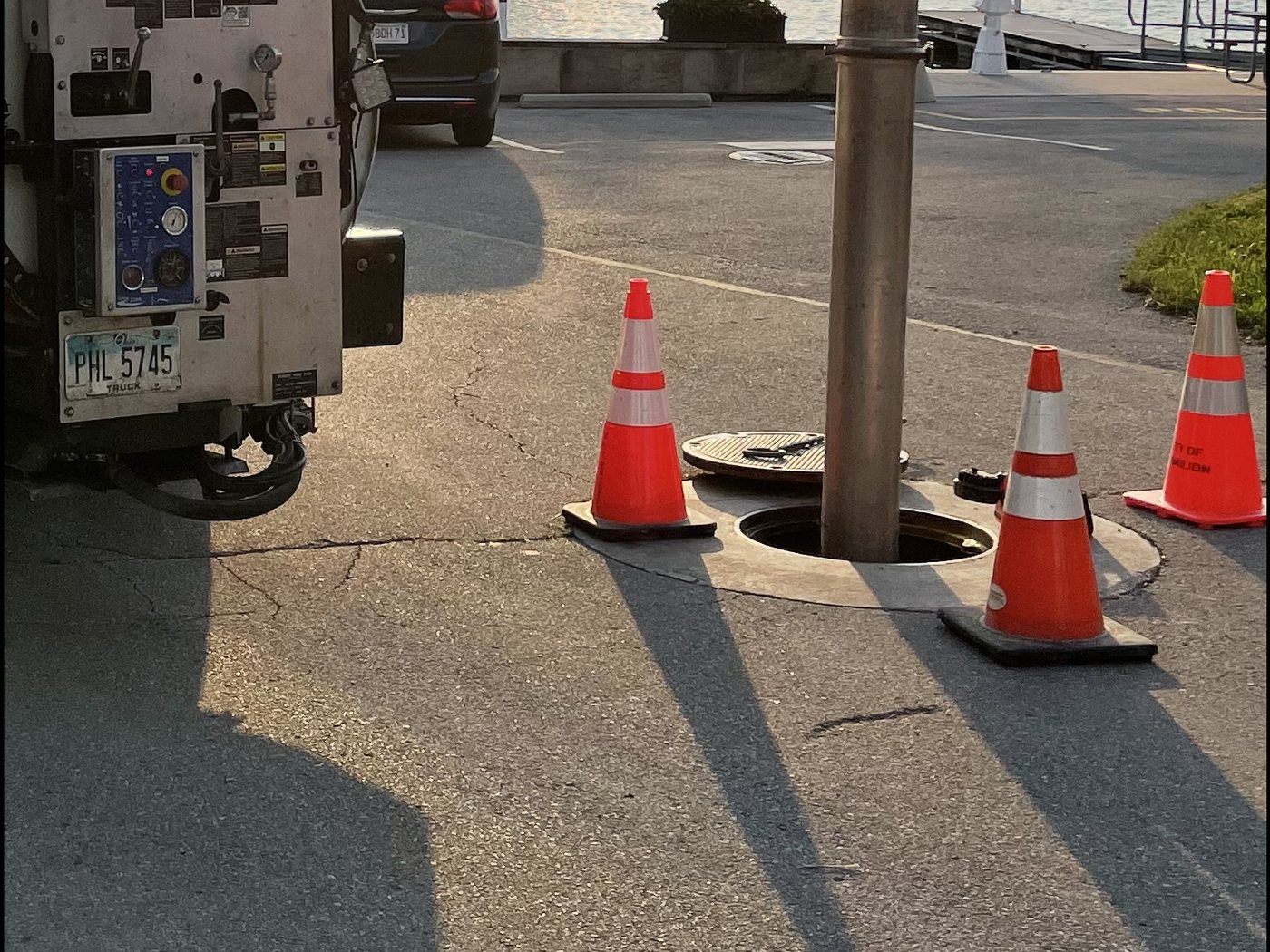 An open sewer manhole with the vacuum tube of a Darr's combination truck lowered into it, traffic cones set around the opening